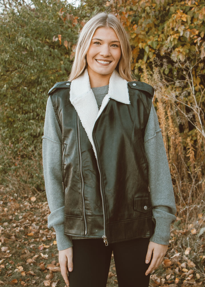 Woman wearing a green vest with white fur lining in an outdoor setting.