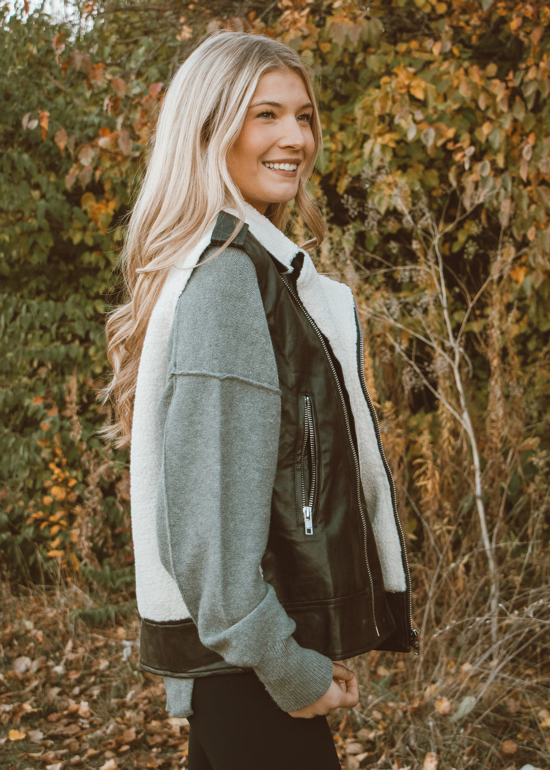 Woman wearing a gray jacket with leather sleeves in an autumn setting