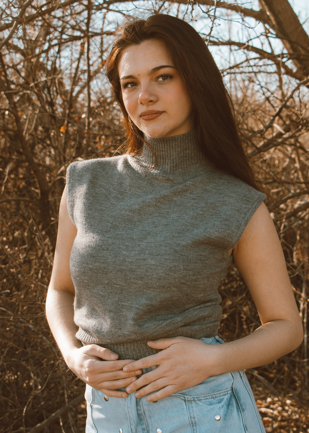 Woman wearing a sleeveless gray knit top with a blurred natural background