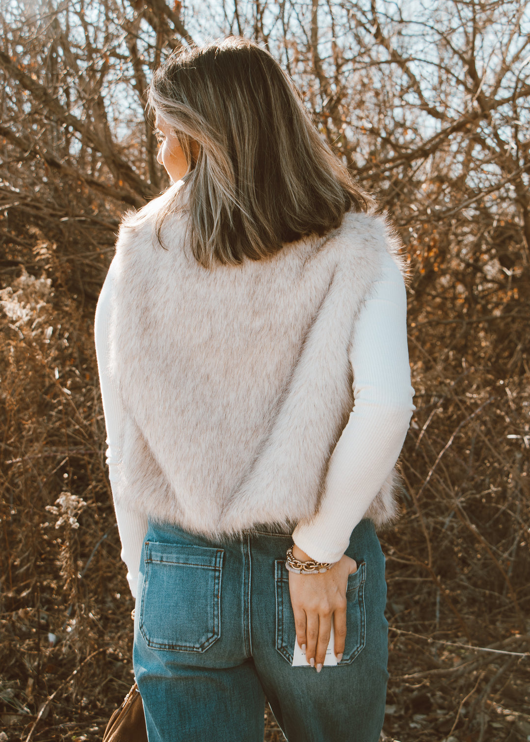 Person wearing a fluffy white sweater and blue jeans standing in a natural setting with trees.