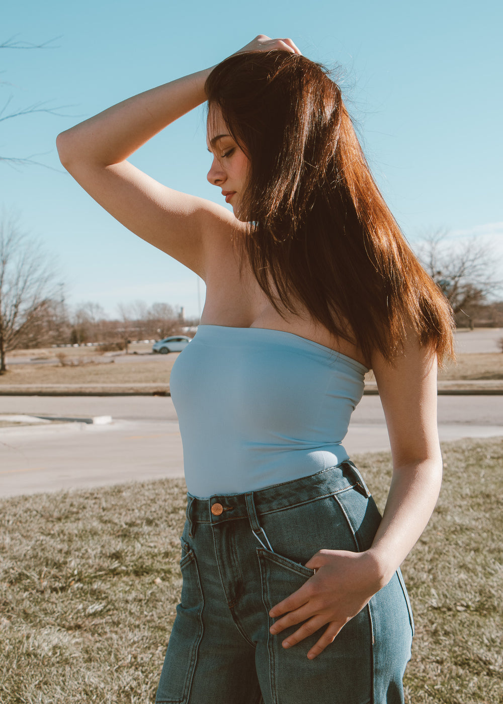 Woman in a light blue strapless top and jeans standing outdoors on a sunny day.