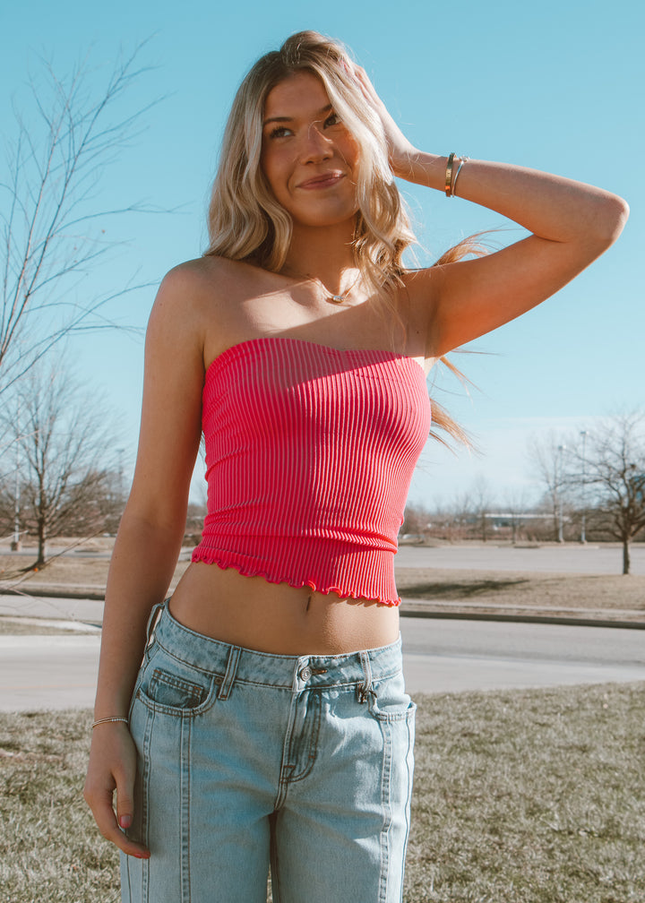 Woman wearing a pink top and blue jeans standing outdoors on a clear day.