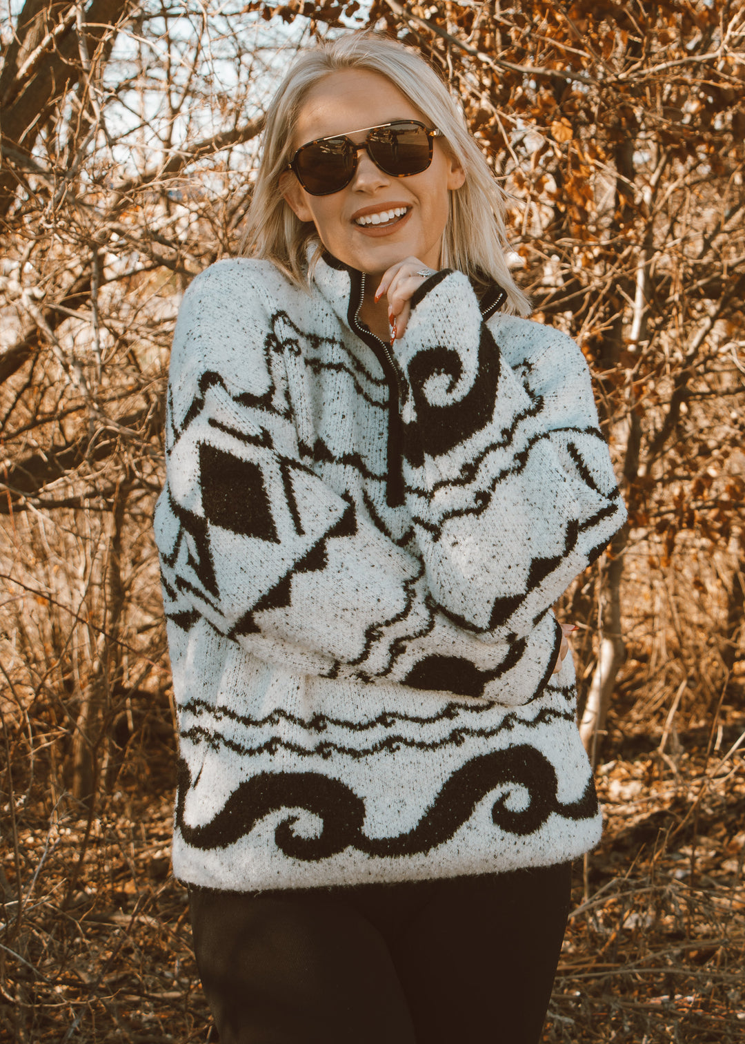 Woman wearing a patterned sweater and sunglasses in a forest setting