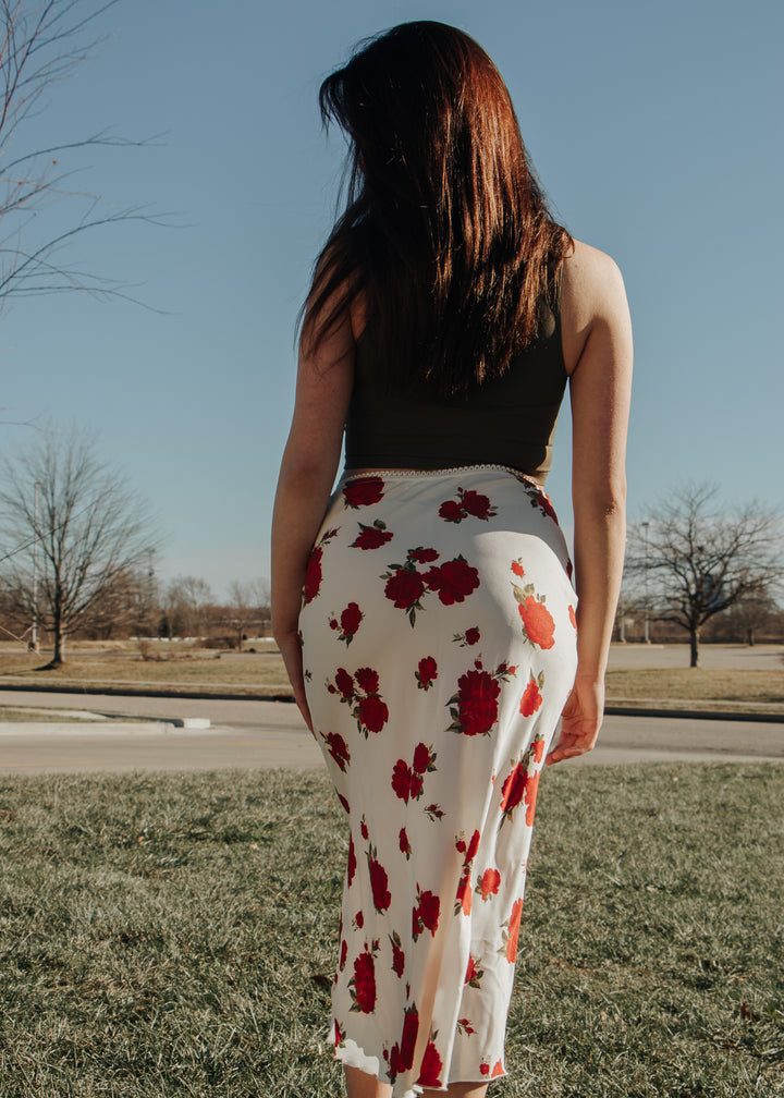 Woman wearing a black top and floral skirt standing outdoors with a clear sky.