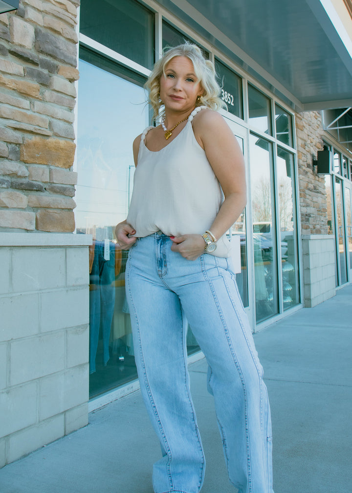Woman in a white top and light blue jeans standing outside a building.