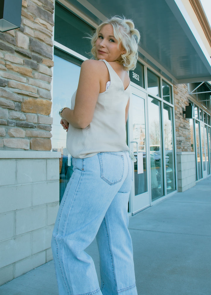 Woman in a white top and light blue jeans standing on a sidewalk with a building in the background