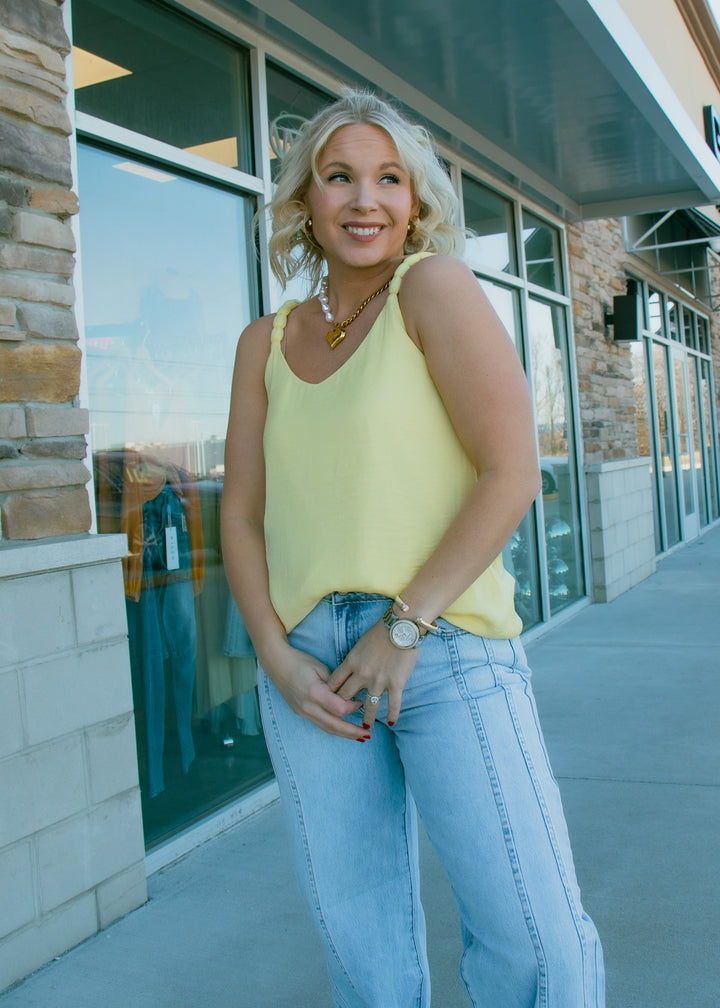 Woman in a yellow top and blue jeans standing outside a building with large windows.
