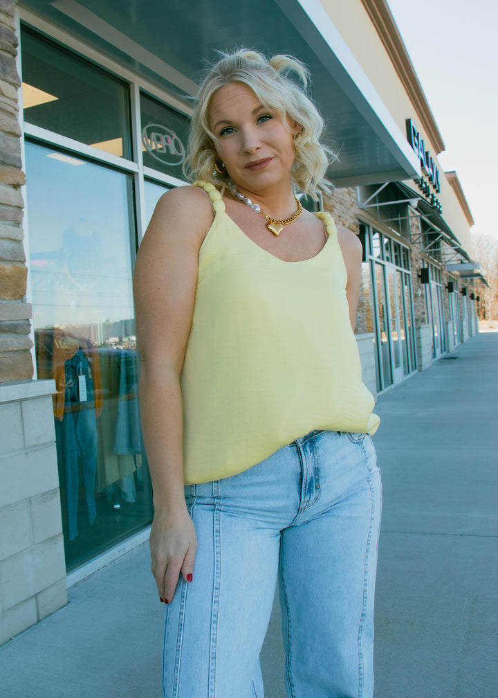 Woman in a yellow top and blue jeans standing on a sidewalk with a store in the background