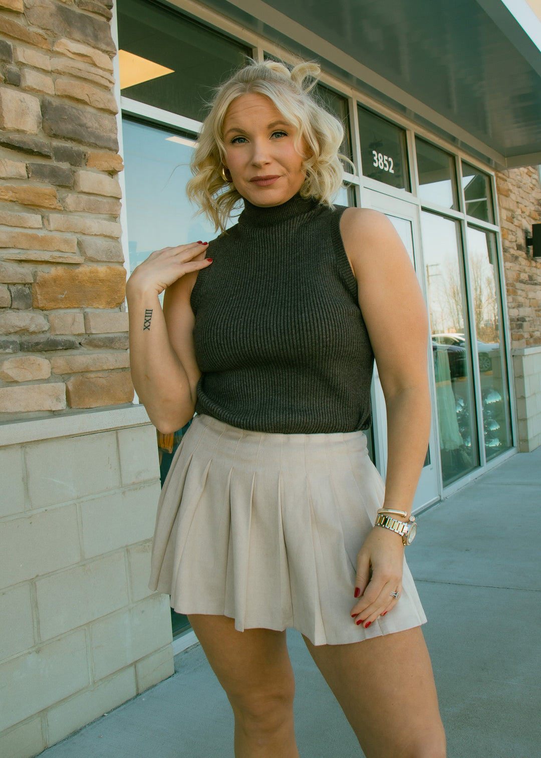 Woman wearing a black turtleneck and beige skirt standing in front of a building.