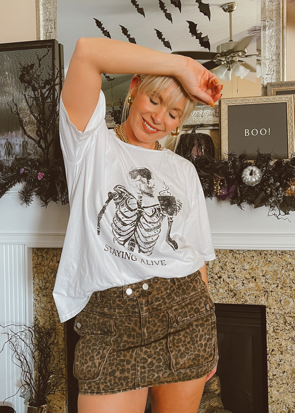 Person wearing a white t-shirt with a skeleton design and leopard print skirt in a Halloween-themed room.