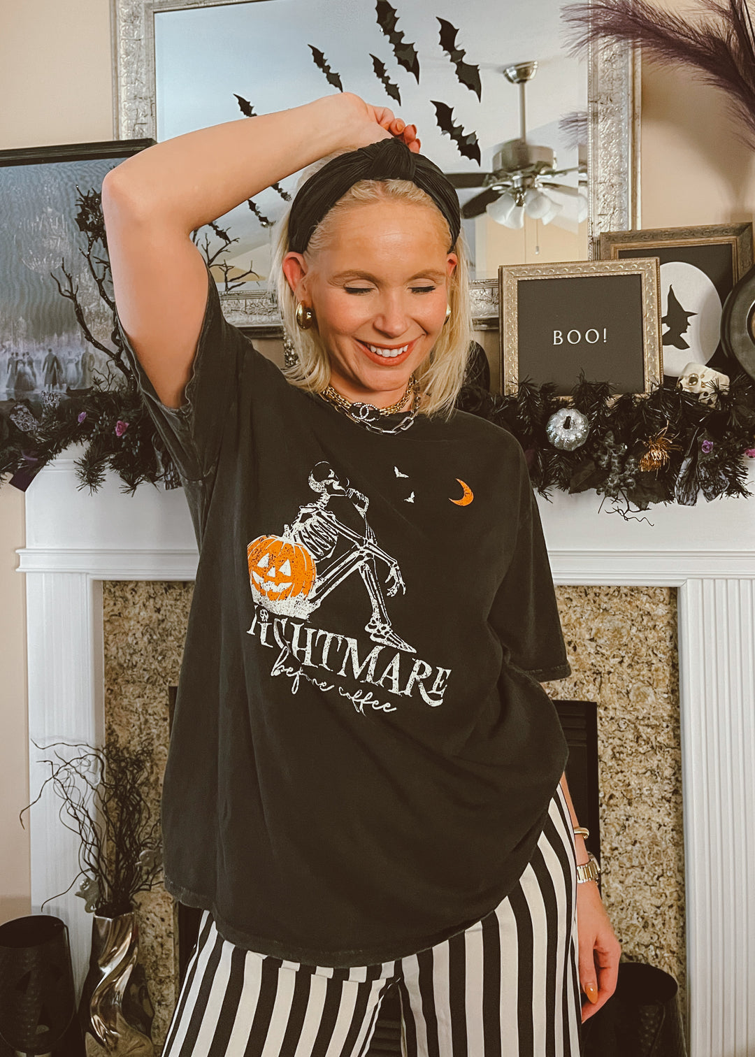 Person wearing a black Halloween-themed t-shirt with striped pants in a decorated room.