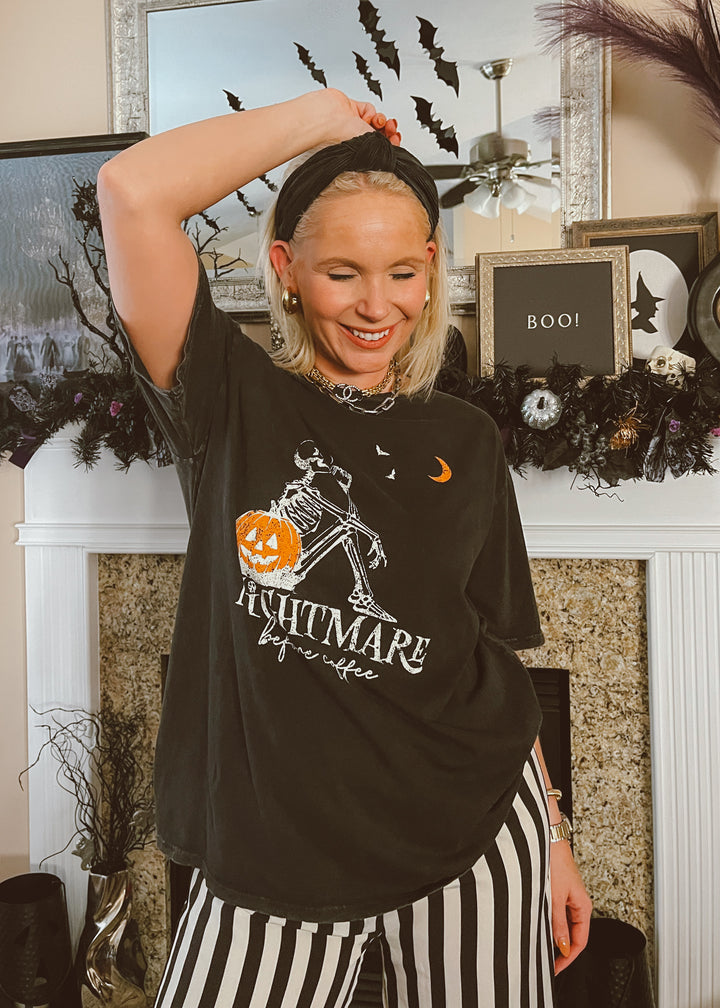 Person wearing a black Halloween-themed t-shirt with striped pants in a decorated room.