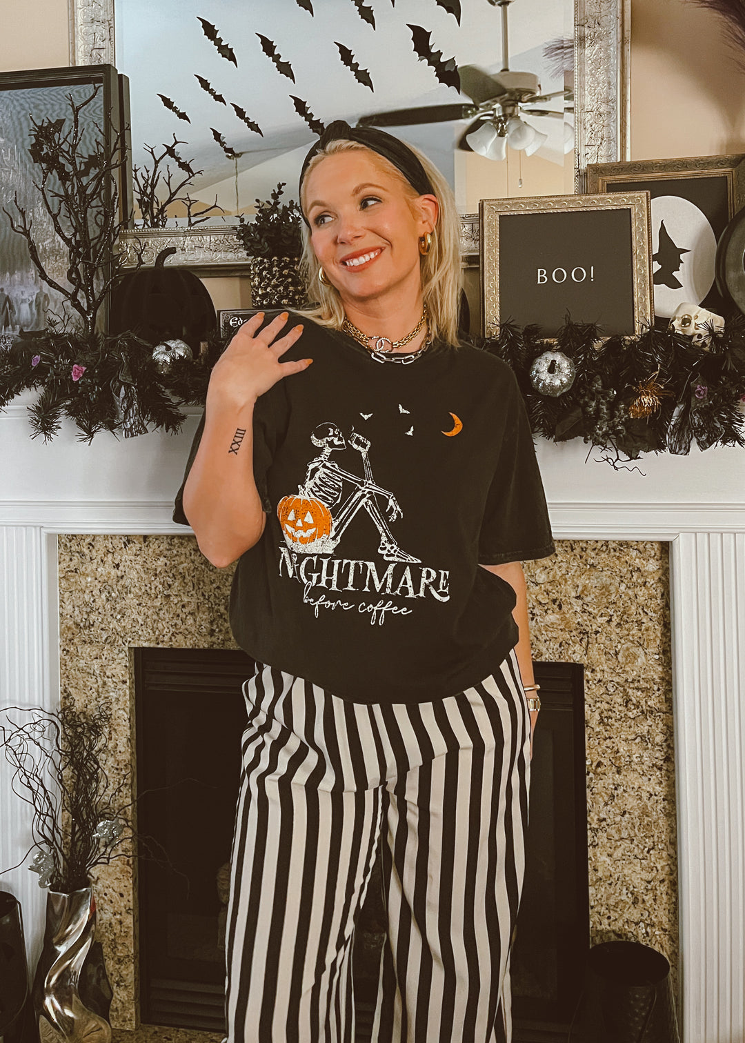Person wearing a Halloween-themed t-shirt and striped pants in front of a decorated fireplace.