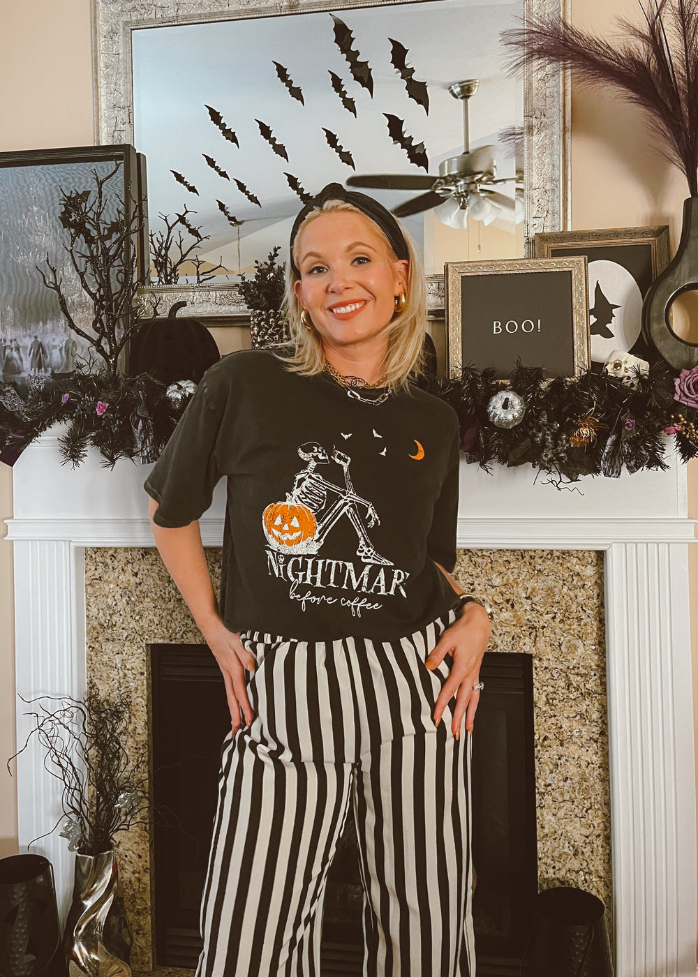 Woman wearing a Halloween-themed shirt and pants in front of a decorated fireplace.