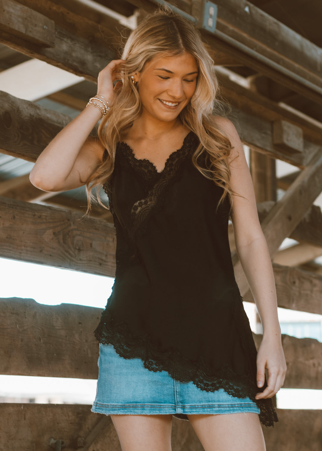 Woman wearing a black lace top and denim skirt standing under wooden beams.