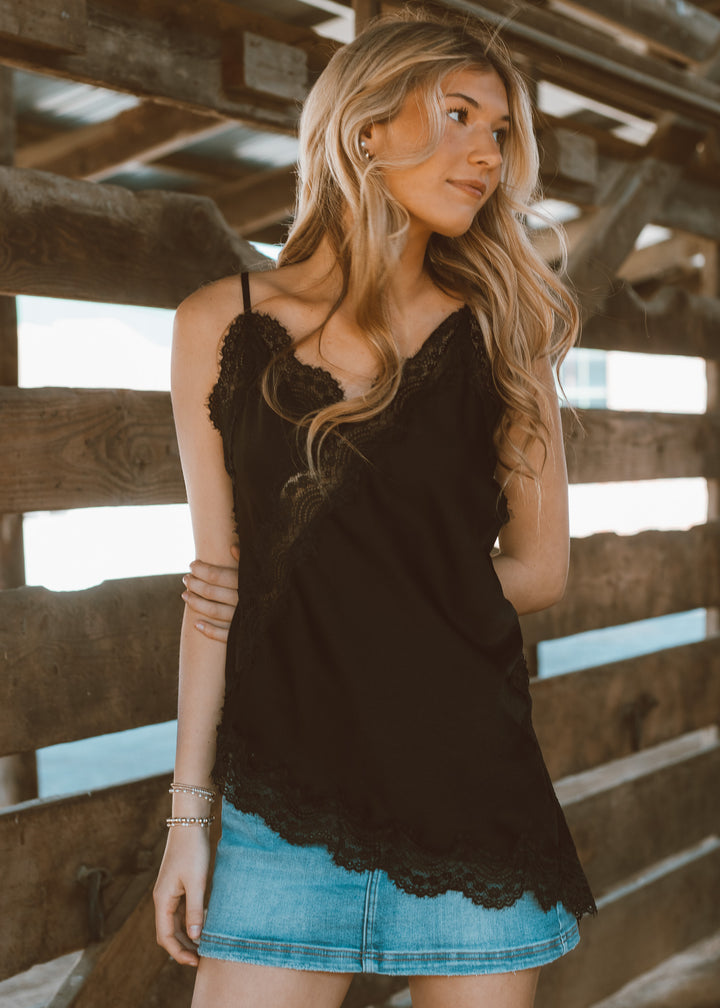 Woman wearing a black lace top and denim skirt standing in front of wooden beams.