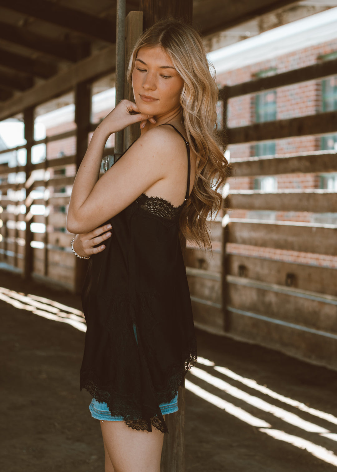 Woman in a black lace top and denim shorts standing in a rustic setting with wooden beams.
