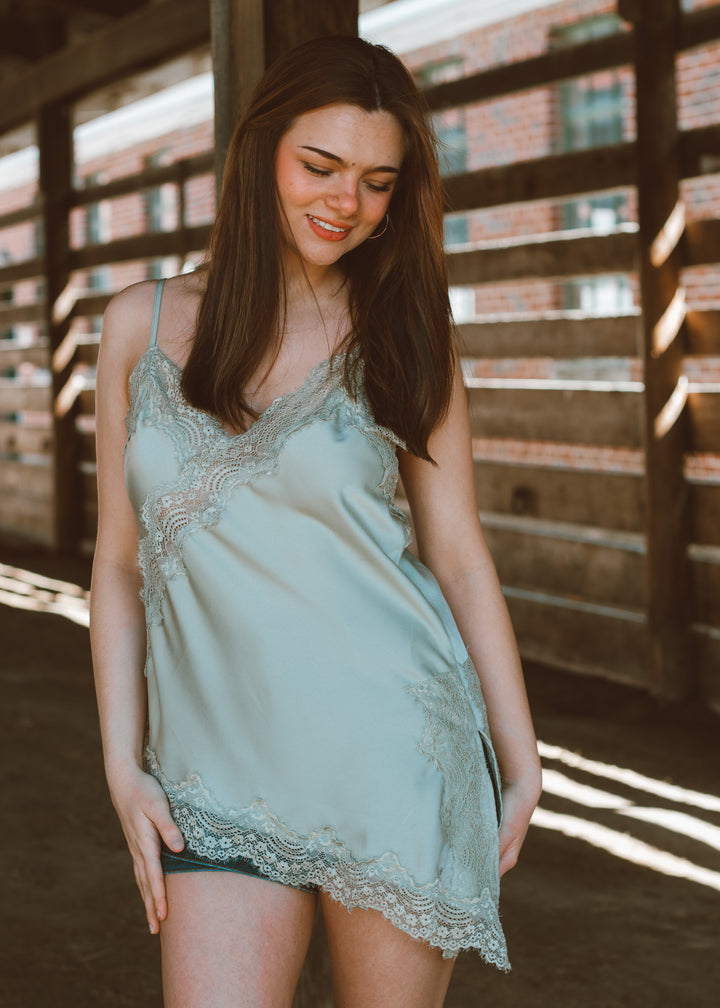 Woman wearing a light green lace nightgown in a rustic setting.