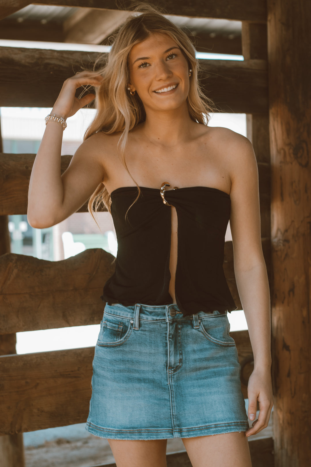 Woman wearing a black strapless top and denim skirt standing in a wooden interior.