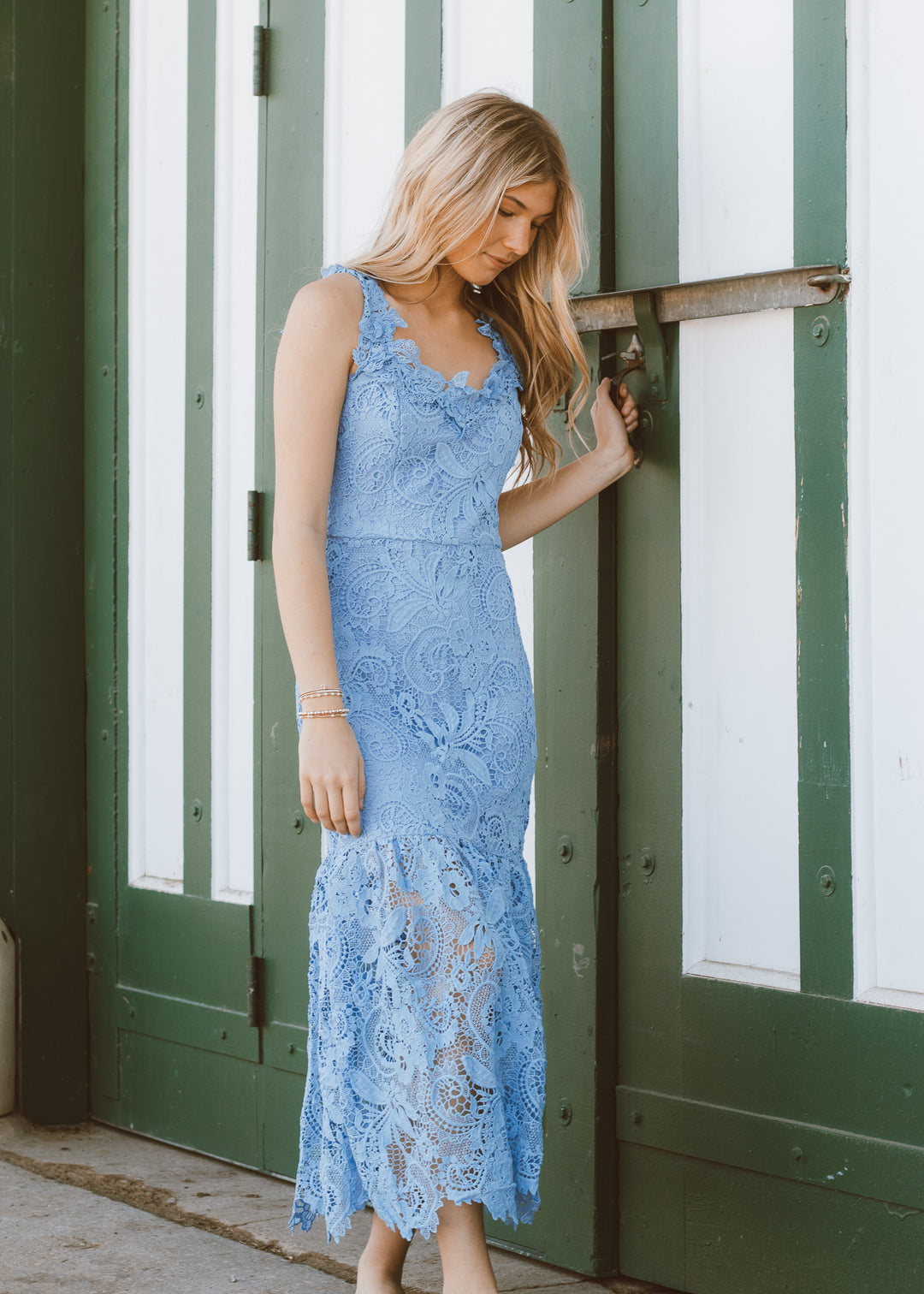 Woman in a blue lace dress standing in front of a green and white striped door.