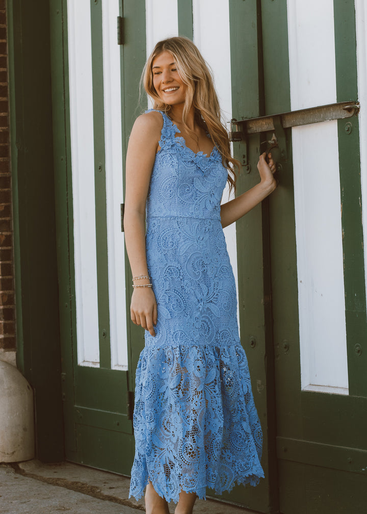 Woman in a blue lace dress standing in front of a green and white striped wall.