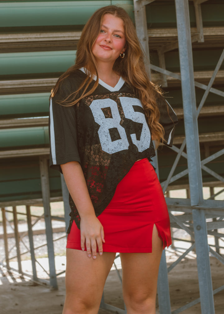 Woman wearing a sports jersey with the number 85 and a red skirt in an outdoor setting.