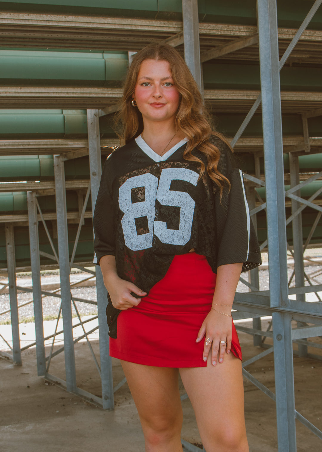 Woman wearing a sports jersey with the number 85 and a red skirt in an outdoor setting.