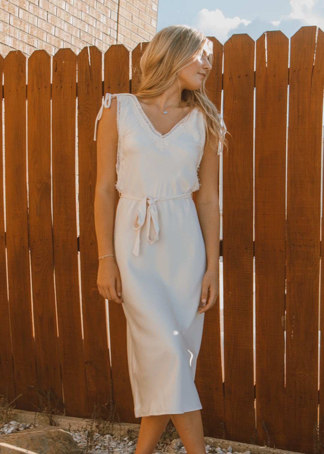 Woman in a white dress standing against a wooden fence