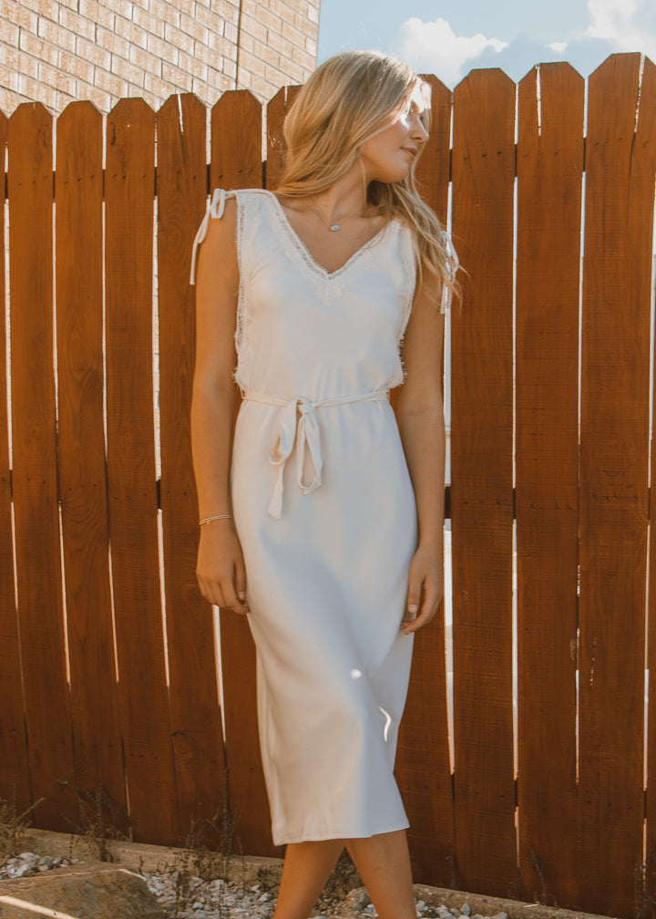 Woman in a white dress standing against a wooden fence