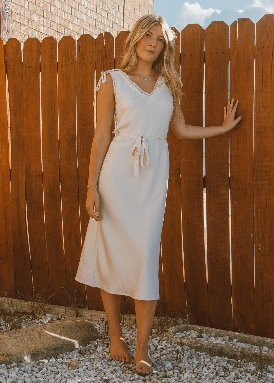 Woman in a white dress standing against a wooden fence.