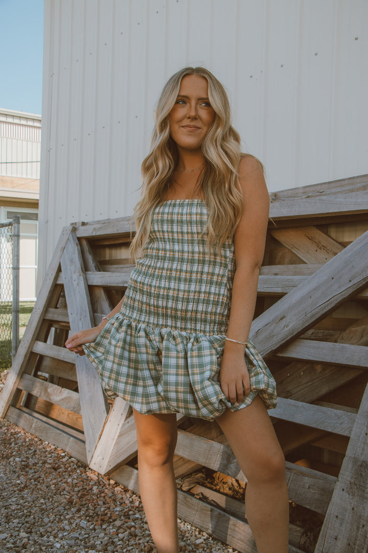 Woman in a plaid dress standing on wooden steps with a white building in the background