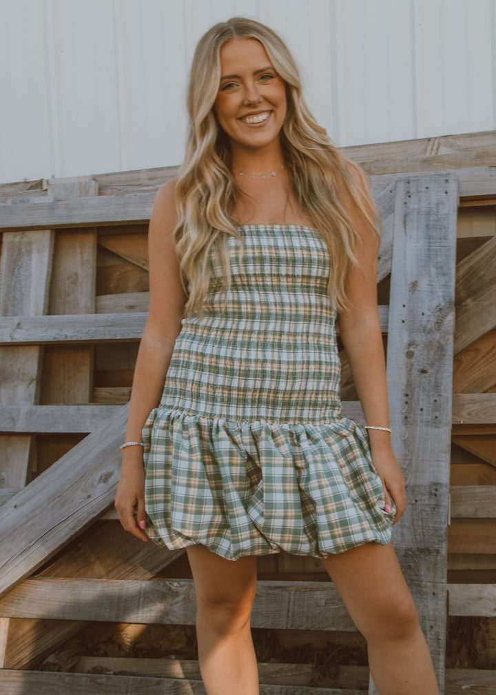 Woman wearing a plaid dress standing in front of a wooden fence.