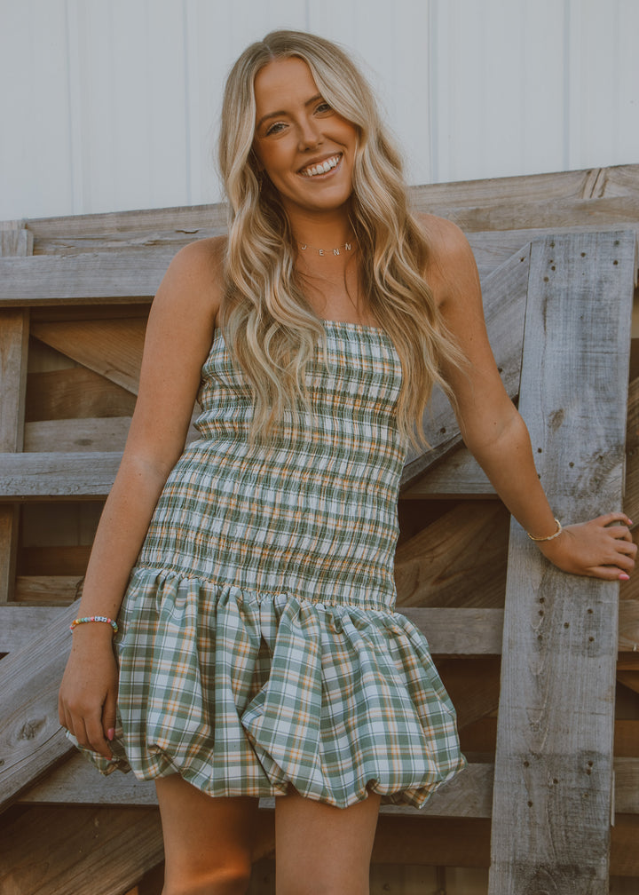 Woman in a plaid dress standing against a wooden background