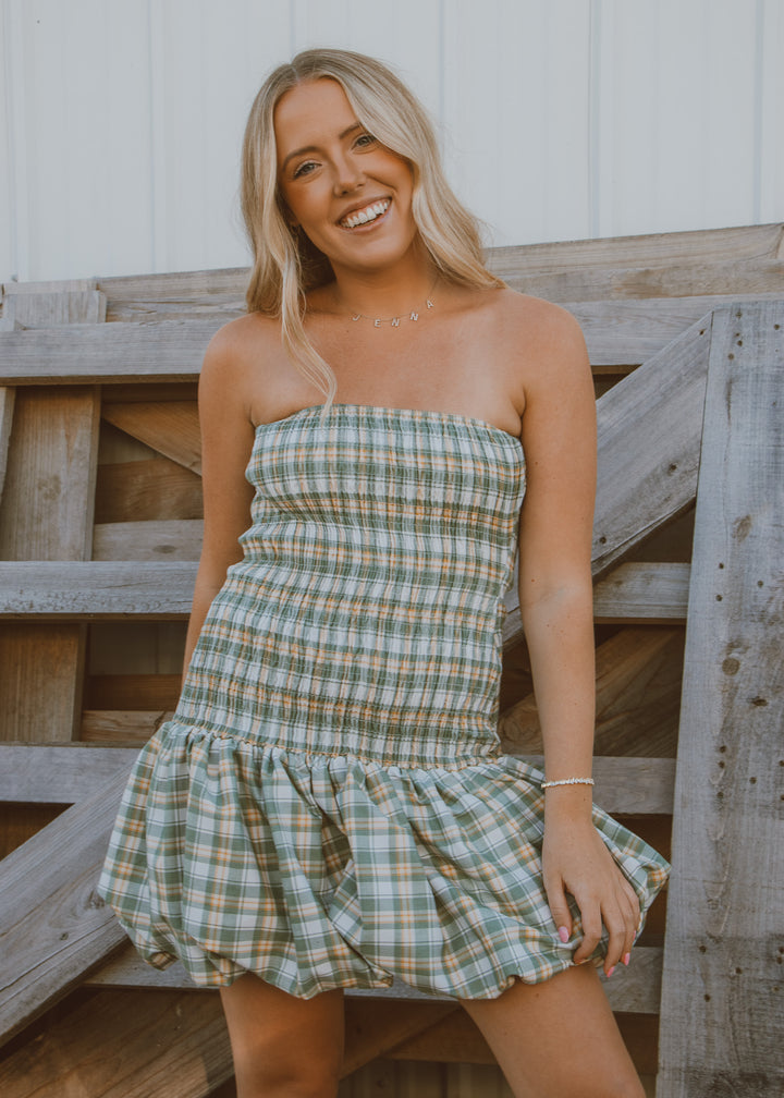 Woman wearing a plaid dress sitting against a wooden fence.