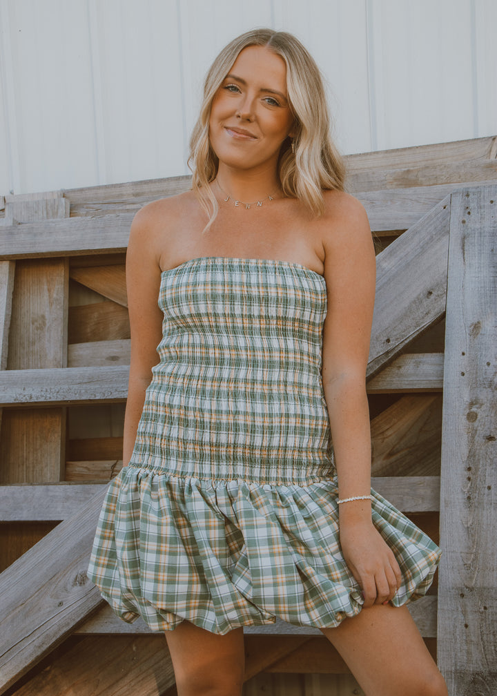Woman wearing a plaid dress standing against a wooden fence.