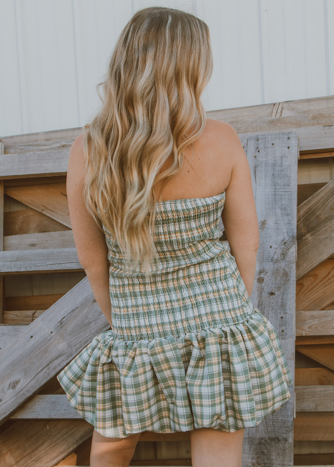 Woman wearing a plaid dress standing against a wooden fence.