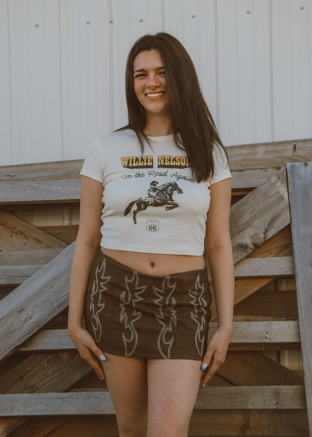 Woman wearing a white t-shirt with graphic design and brown shorts standing on wooden steps.