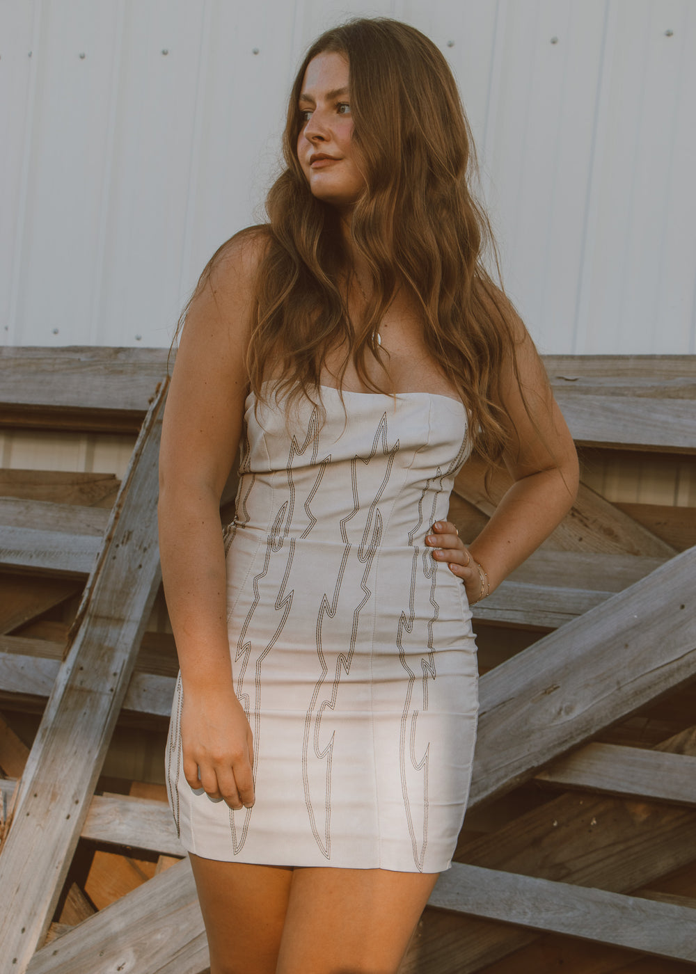 Woman wearing a strapless dress with a pattern, standing on wooden steps.