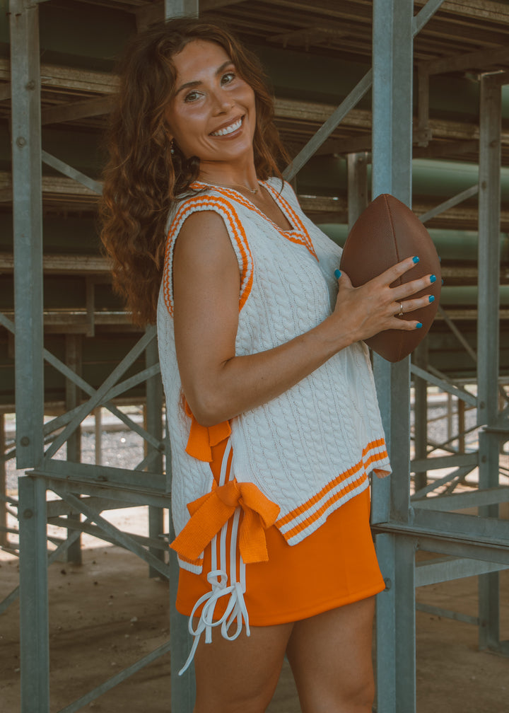 Woman in an orange and white dress holding a football outdoors.