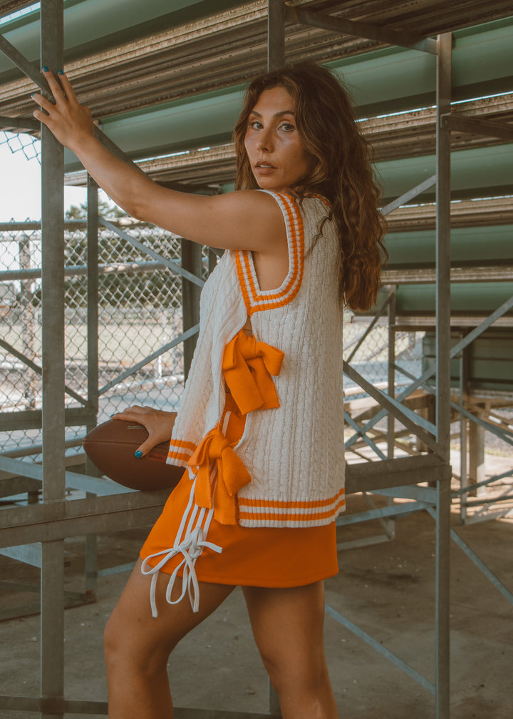 Woman in a white and orange dress standing on metal scaffolding.