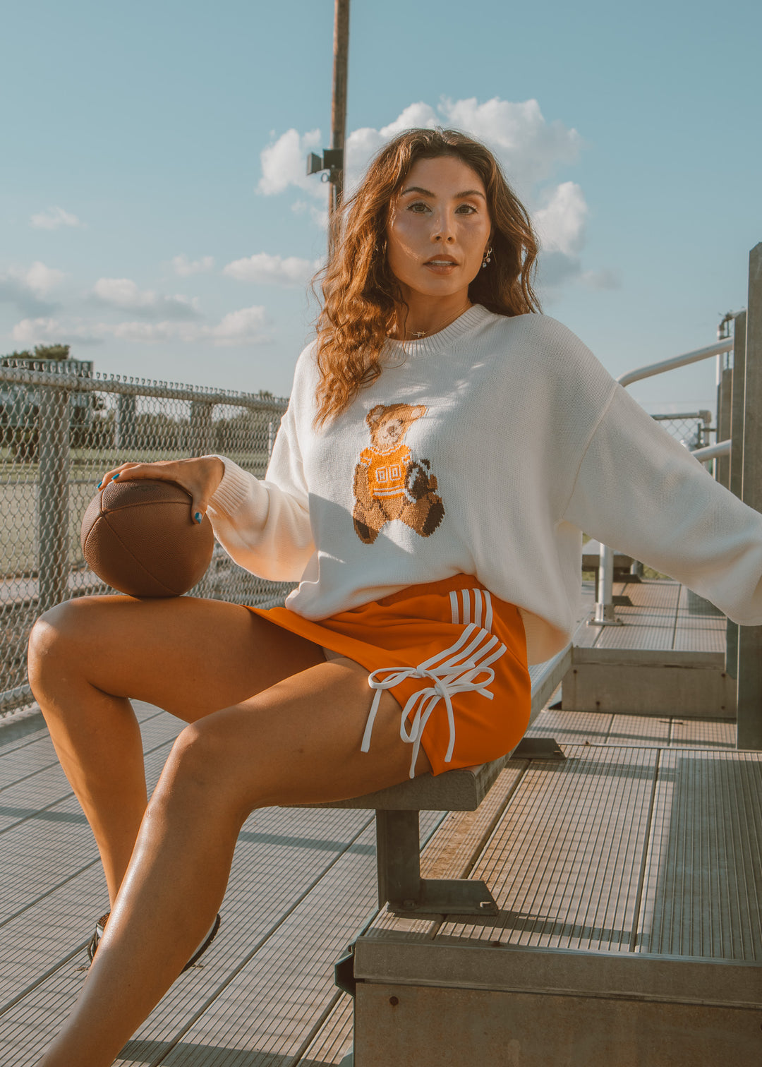 Woman wearing an orange skirt with line detailing and bow details holding a football 
