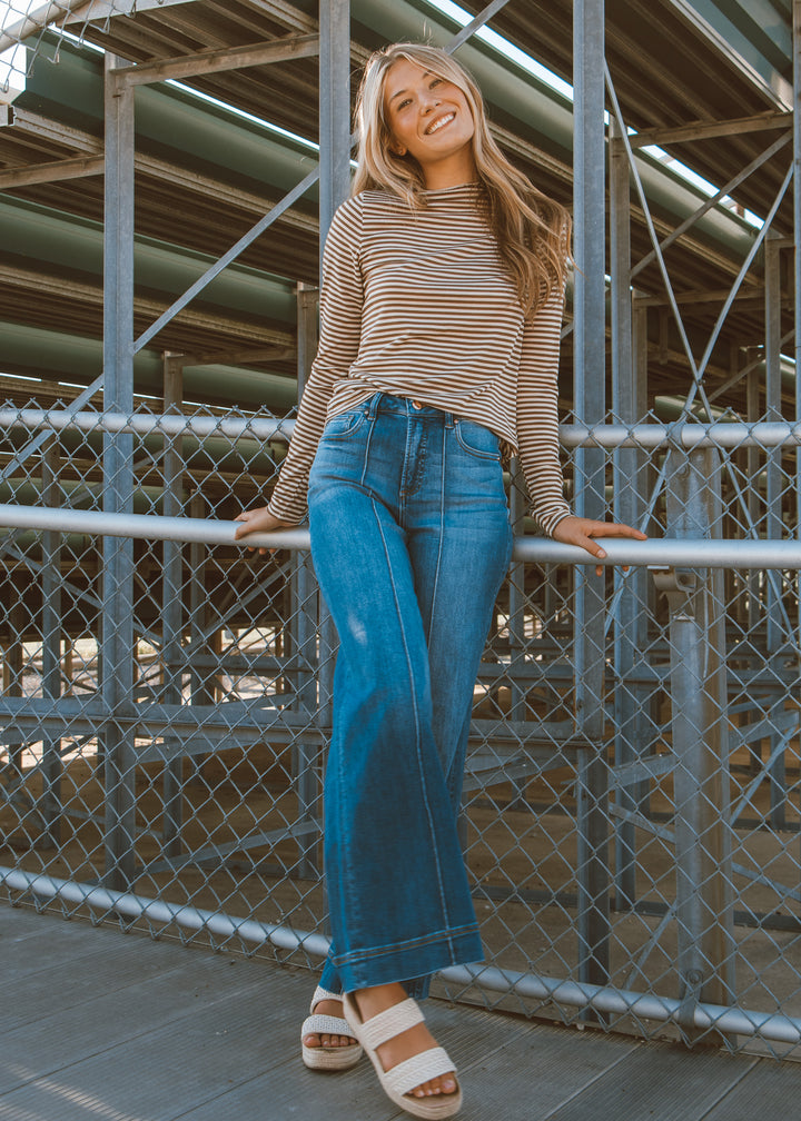 Woman in striped shirt and blue jeans leaning against a metal railing.