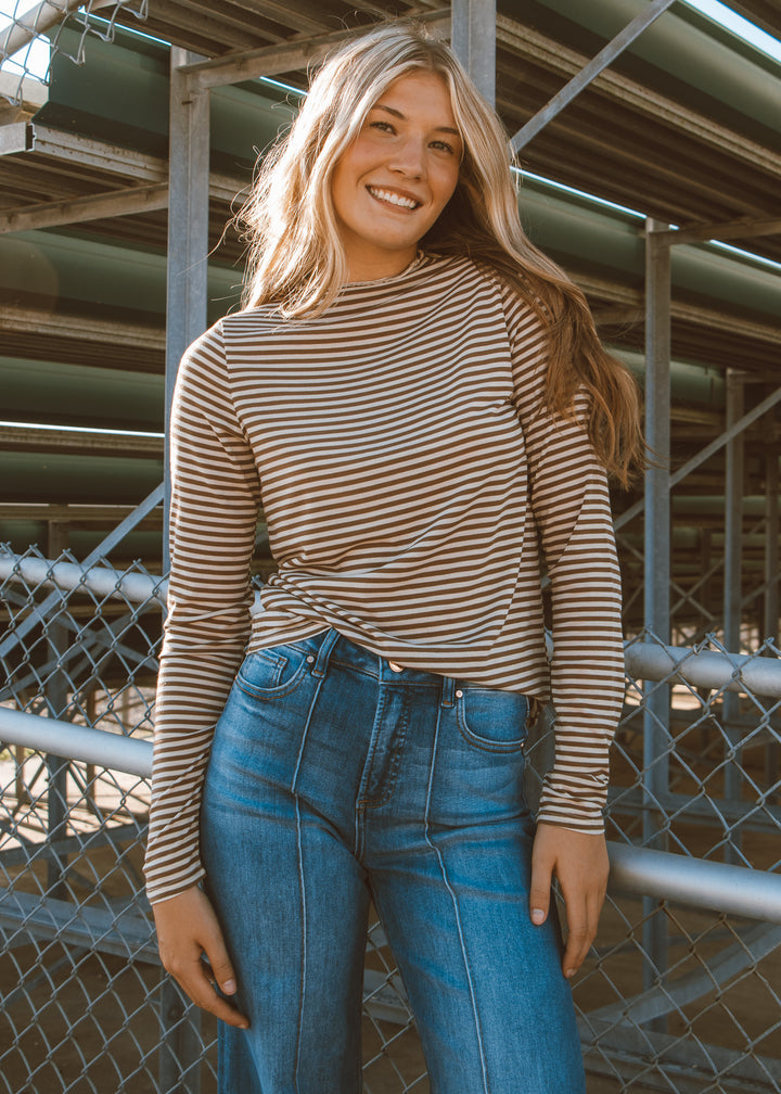 Woman wearing a striped shirt and blue jeans standing in front of a metal fence.