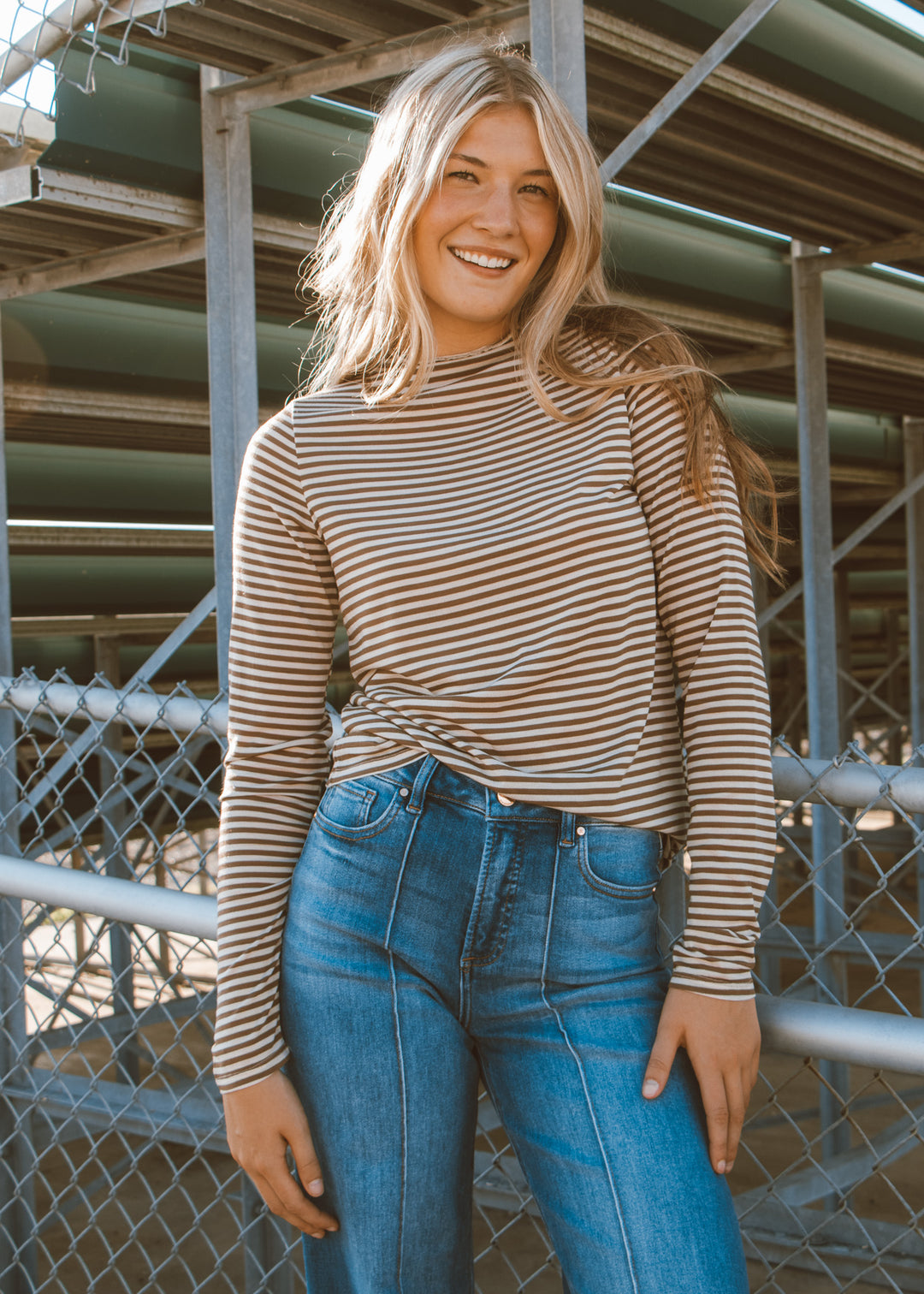 Woman wearing a striped long-sleeve top and blue jeans standing in front of metal railings.