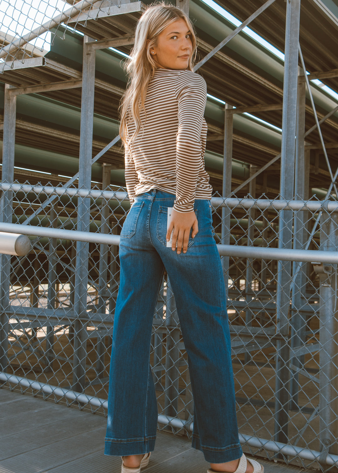 Woman wearing a striped shirt and blue jeans standing on a bridge.