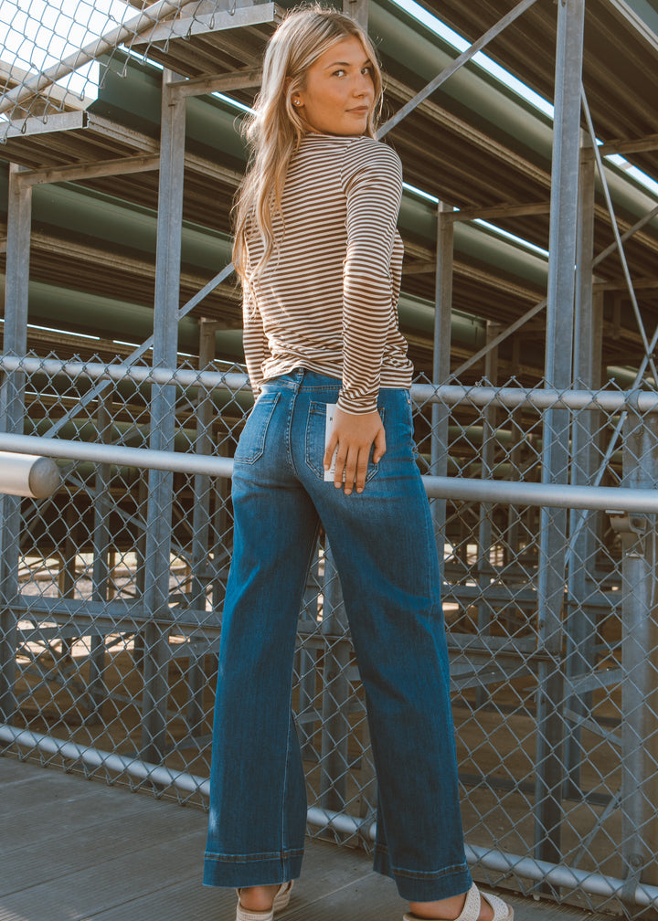 Woman wearing a striped shirt and blue jeans standing on a bridge.