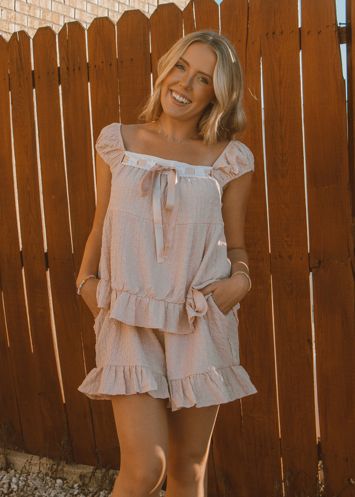Woman wearing a light pink dress standing in front of a wooden fence.
