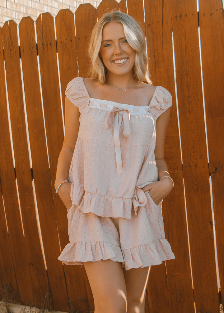 Woman wearing a light-colored dress standing against a wooden fence.