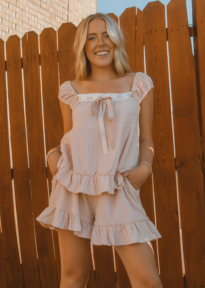 Woman wearing a light-colored dress with ruffles against a wooden fence.