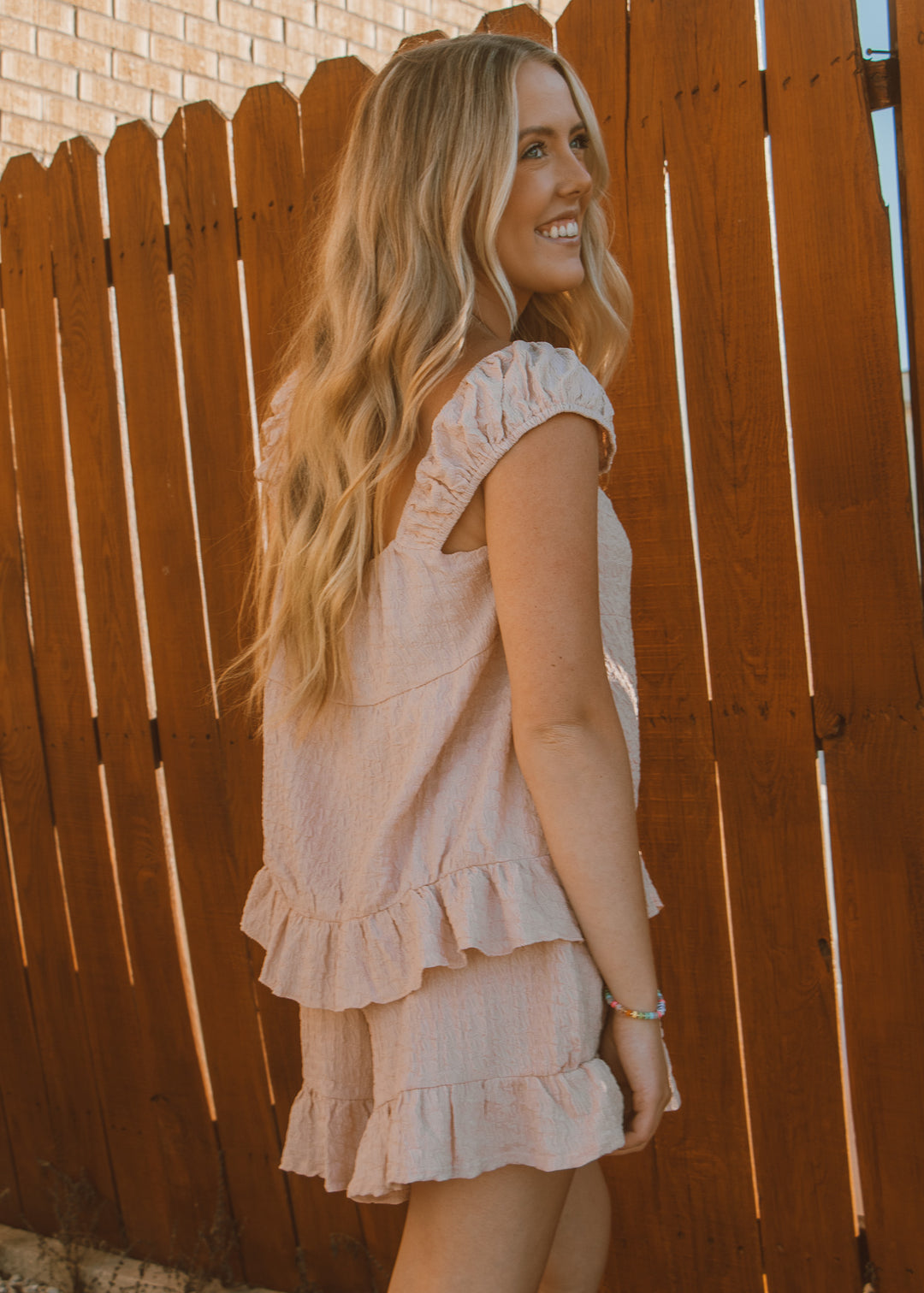 Woman in a light pink dress standing against a wooden fence